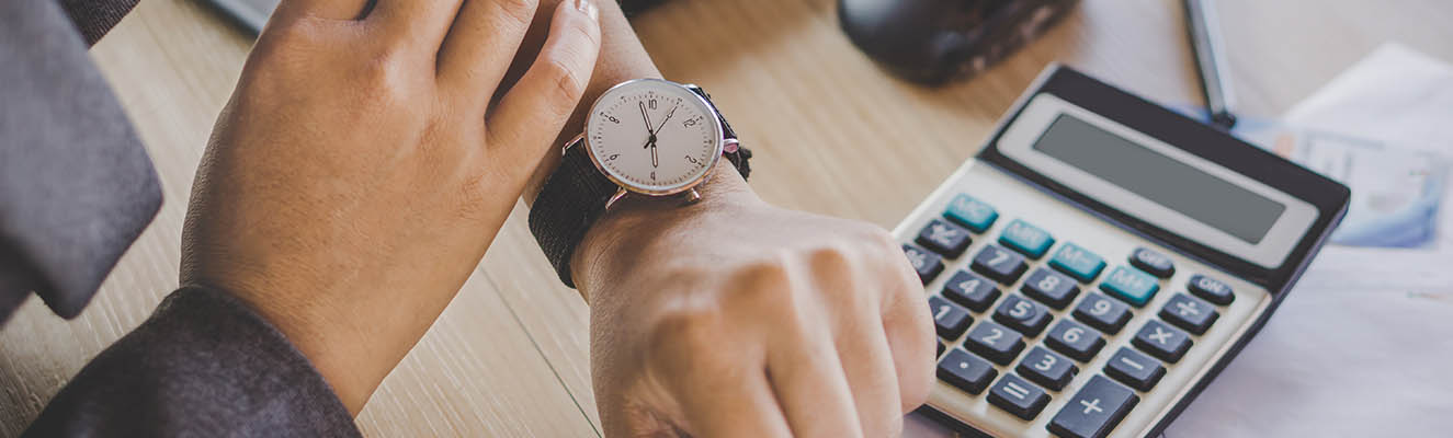 man looking at watch and a calculator on desk