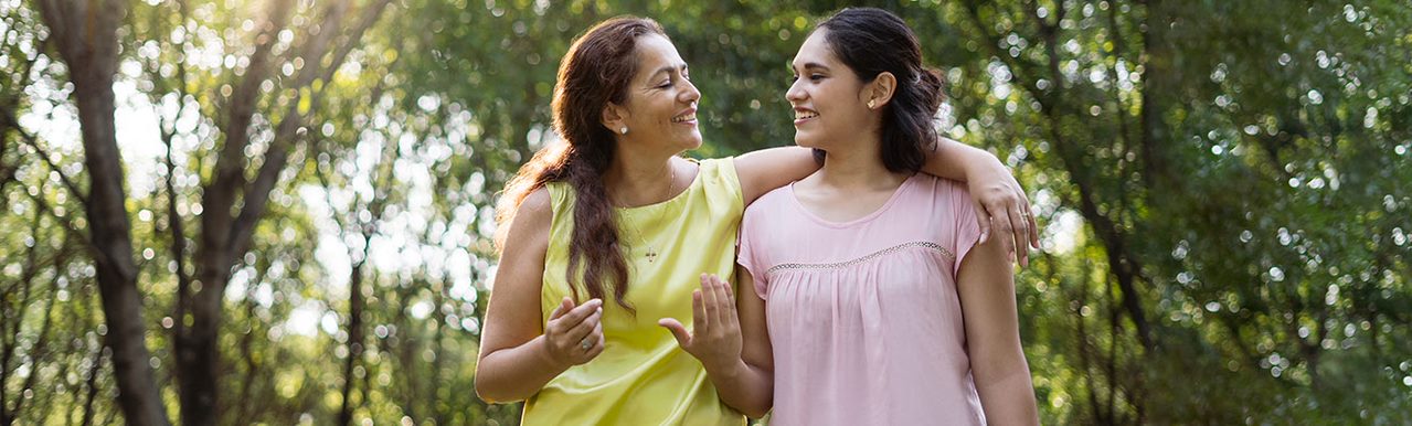 A mother standing with her arm around her daughter smiling