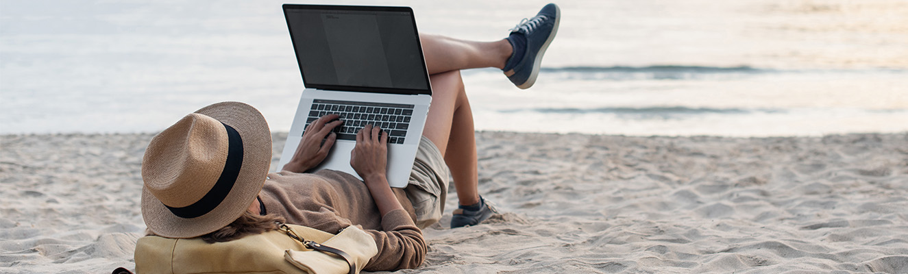 Man laying on a beach on typing on a laptop