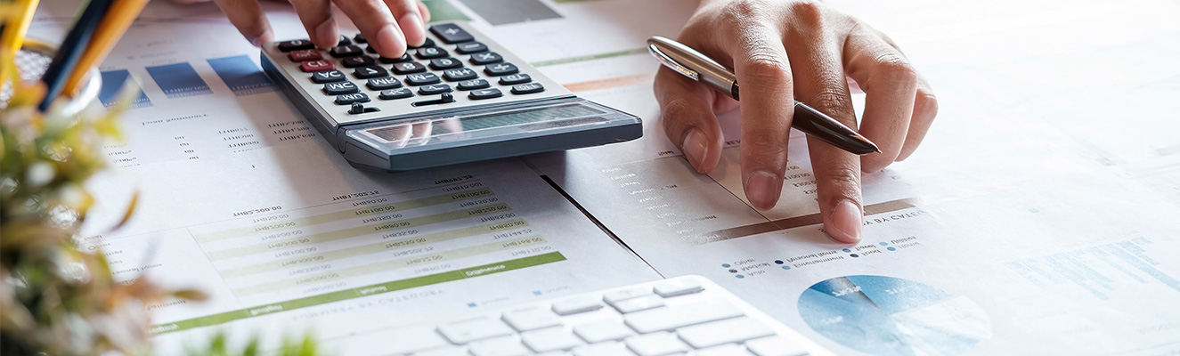The article featured image showing a person calculating rates - right hand on and left hand with a pen checking calculator data on papers with graphs and numbers