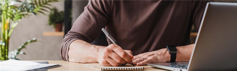man writing in front of a laptop