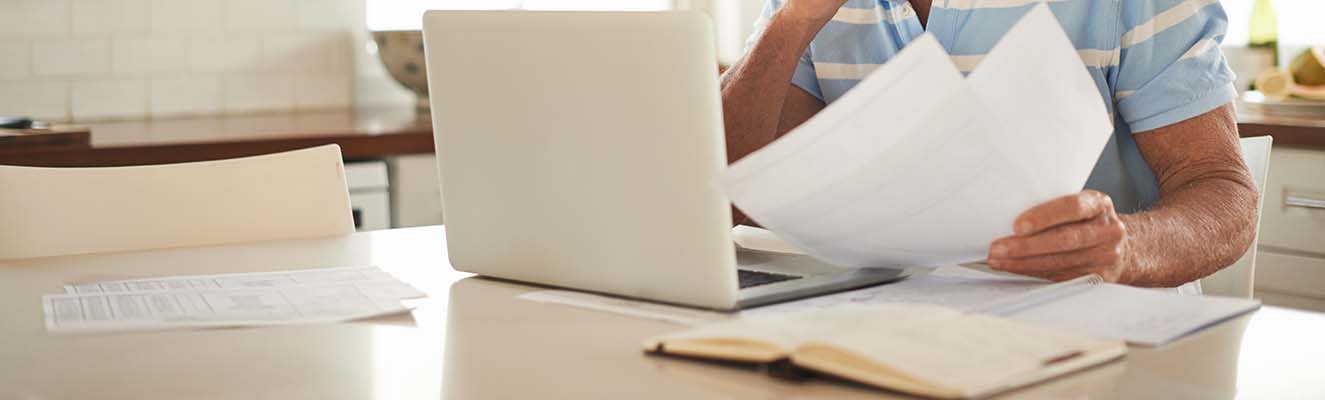 Man looking at paperwork and laptop